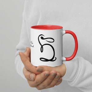 May include: White ceramic mug with a red rim and handle. The mug features a black line drawing of a rabbit with the text "Don't be the  " and "understand." printed on the mug.