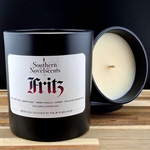 May include: Black scented candle with a white label featuring the text "Southern Novelscents Fritz". The candle is 8 oz (226g) and has a wooden wick. The scent includes Earl Grey Tea, Lemon Zest, and Amber.