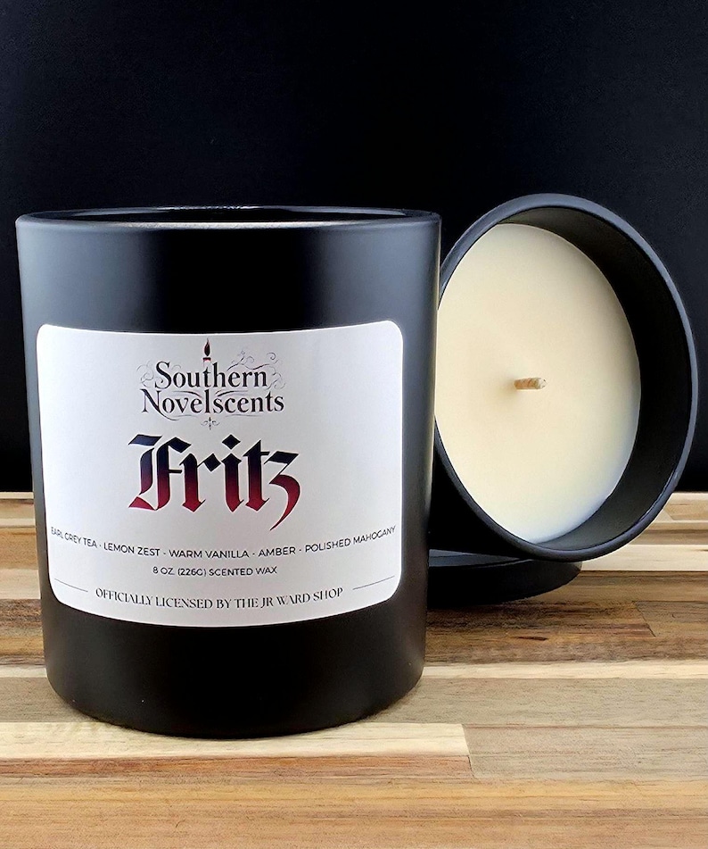 May include: Black scented candle with a white label featuring the text "Southern Novelscents Fritz". The candle is 8 oz (226g) and has a wooden wick. The scent includes Earl Grey Tea, Lemon Zest, and Amber.