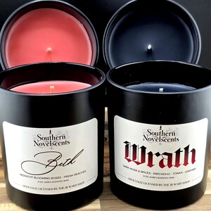 May include: Two black scented candles with lids off, revealing red and dark blue wax. The labels read "Beth" and "Wrath" with scent descriptions. The candles are 8 oz (226g) each.