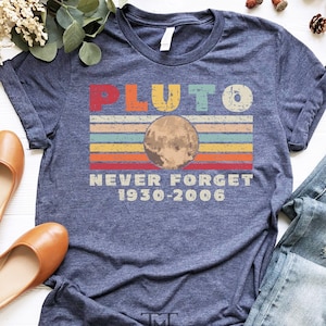 May include: A navy blue t-shirt with a vintage-style graphic of Pluto, the planet, with the text "Pluto Never Forget 1930-2006".