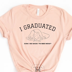 以下が含まれることがあります： 薄いピンクのTシャツに、黒い文字で「卒業しました。もう寝てもいいですか？」と書いてあり、寝ている人の線画が描かれています。