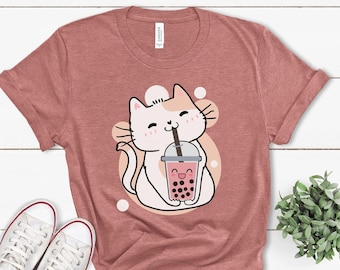 May include: A heather mauve t-shirt featuring a cartoon cat drinking bubble tea. The cat is white with orange patches and has a pink nose and pink cheeks. The bubble tea is pink with black boba pearls and a happy face. The t-shirt has the text "Heather Mauve" printed on the bottom.
