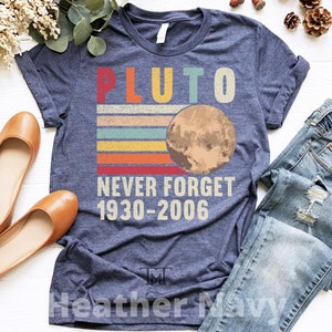 May include: A heather navy blue t-shirt with a vintage-style graphic of Pluto, the text "Pluto Never Forget 1930-2006", and the text "Heather Navy" at the bottom.