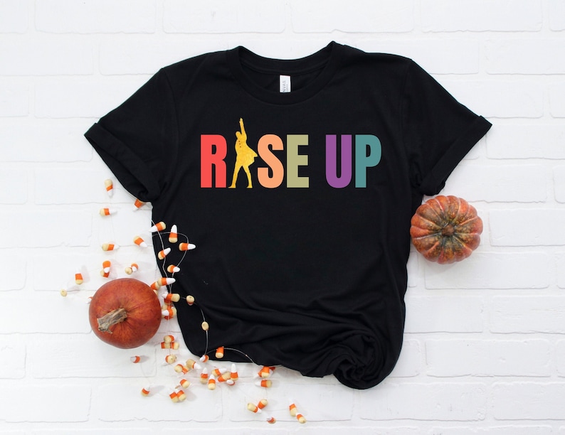 May include: Black t-shirt with a rainbow colored graphic that says "Rise Up" and a silhouette of a person in the middle of the word "Rise".