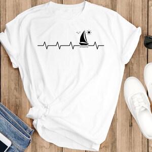 May include: White t-shirt with a black sailboat and sun graphic, a heartbeat line, and the text "Sail Away".