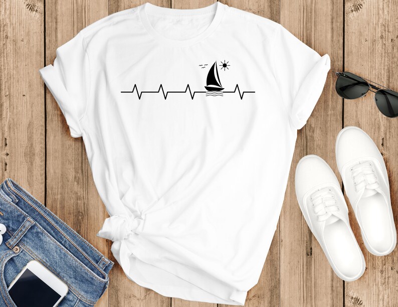 May include: White t-shirt with a black sailboat and sun graphic, a heartbeat line, and the text "Sail Away".