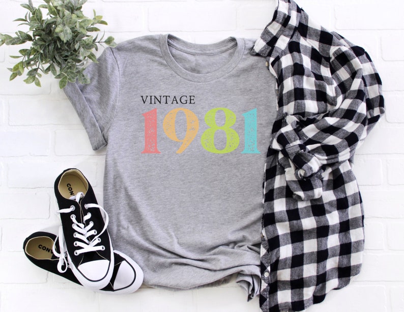 Puede incluir: Camiseta gris con el texto "Vintage 1981" en colores arco&iacute;ris. El a&ntilde;o est&aacute; en una fuente desgastada.