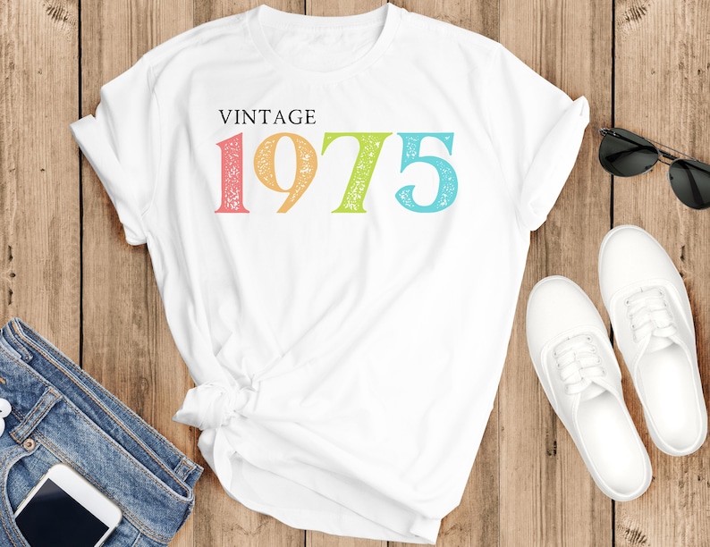May include: White t-shirt with the text "Vintage 1975" in rainbow colors. The numbers are distressed and have a vintage look.