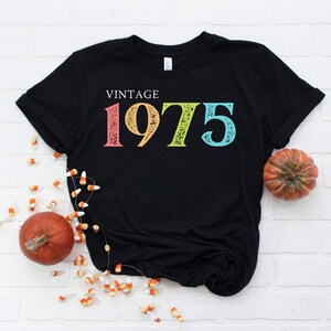 May include: Black t-shirt with the text "Vintage 1975" in rainbow colors. The numbers are distressed and have a vintage look.
