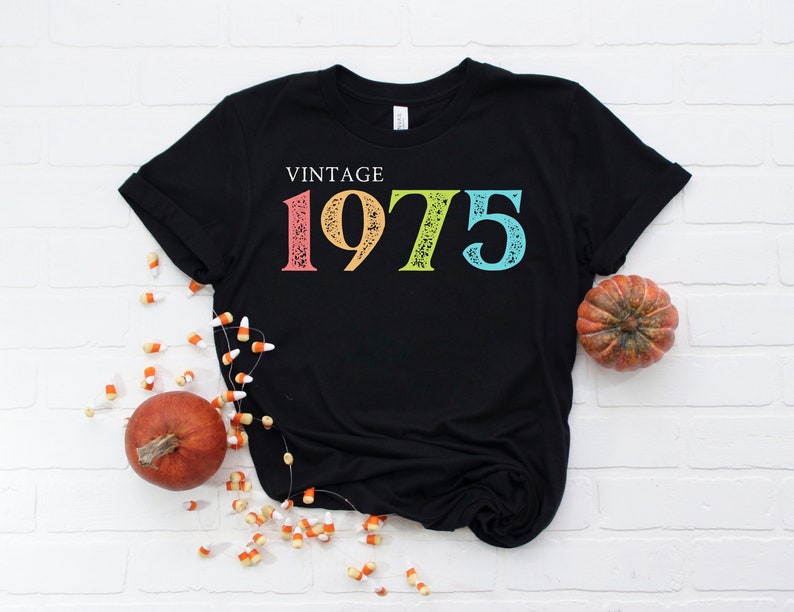 May include: Black t-shirt with the text "Vintage 1975" in rainbow colors. The numbers are distressed and have a vintage look.