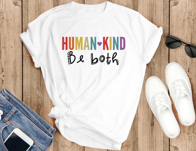 Puede incluir: Camiseta blanca con el texto "HUMAN-KIND Be both" en colores arco&iacute;ris con un coraz&oacute;n morado.