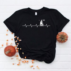 May include: Black t-shirt with a white sailboat graphic and a heartbeat line with a sun and birds above the boat.