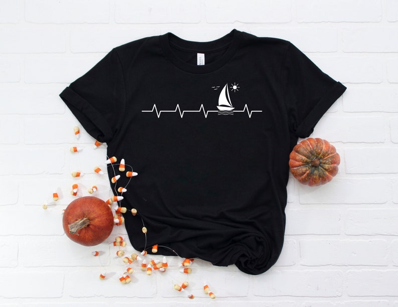 May include: Black t-shirt with a white sailboat graphic and a heartbeat line with a sun and birds above the boat.