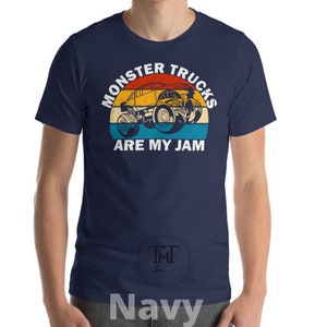 May include: A navy blue t-shirt with a vintage-style graphic of a monster truck. The graphic features a yellow monster truck with a red, orange, and blue background. The text "Monster Trucks Are My Jam" is printed in white below the graphic.