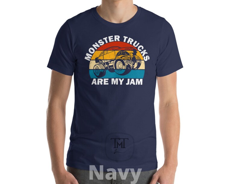 May include: A navy blue t-shirt with a vintage-style graphic of a monster truck. The graphic features a yellow monster truck with a red, orange, and blue background. The text "Monster Trucks Are My Jam" is printed in white below the graphic.