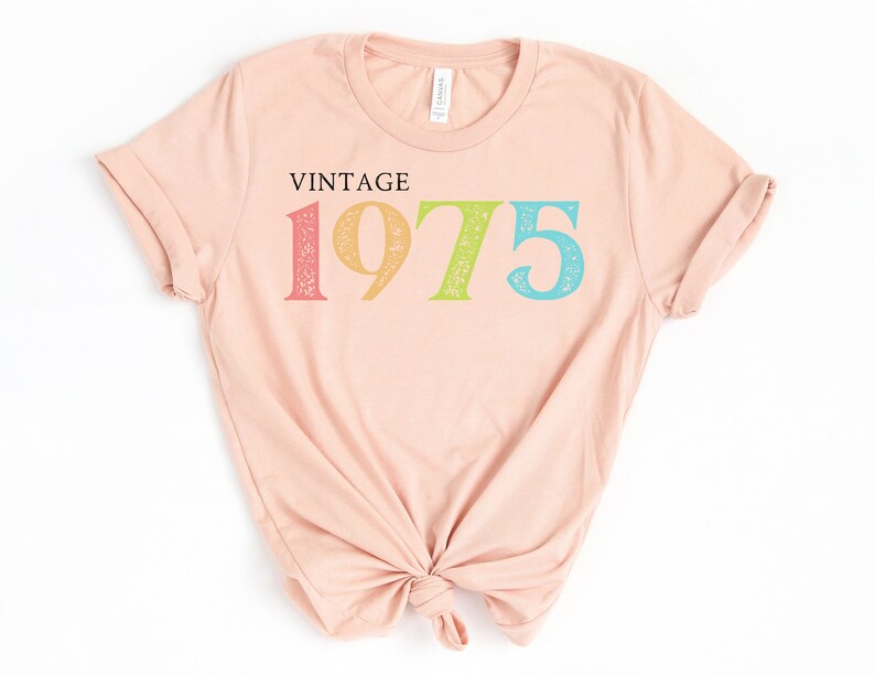 May include: A light pink t-shirt with the text "Vintage 1975" printed on the front in rainbow colors.