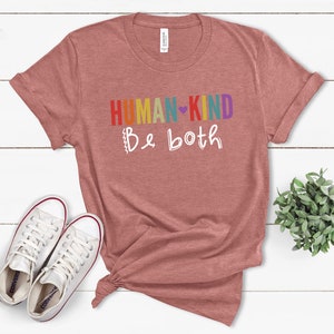 Puede incluir: Una camiseta de color rojo heather con el texto "HUMAN-KIND Be both" en colores arco&iacute;ris y un coraz&oacute;n blanco.