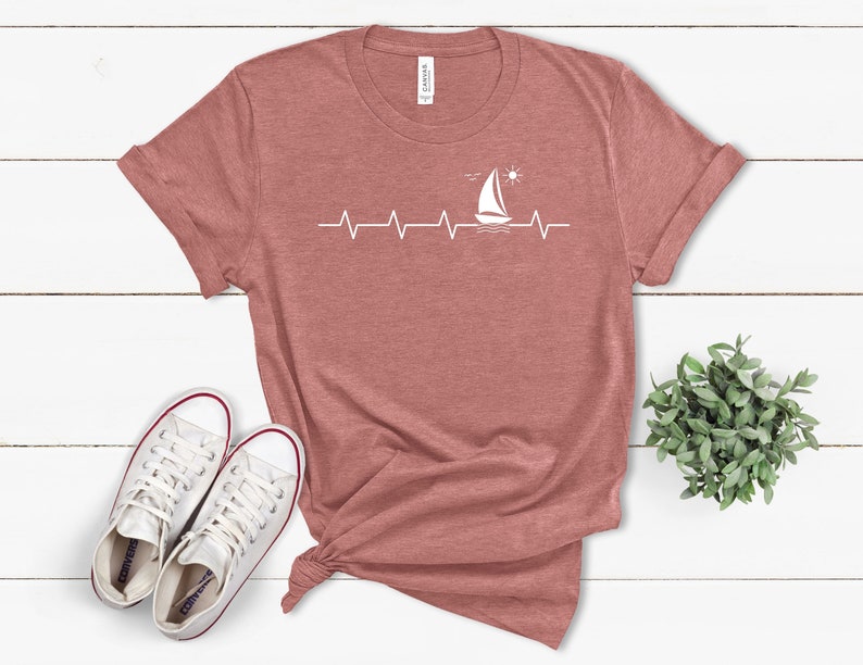 May include: A maroon t-shirt with a white sailboat graphic and a heartbeat line. The sailboat is sailing on a wavy line with a sun above it.