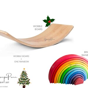 Puede incluir: Un juego de juguetes que incluye una tabla oscilante de madera y un arco&iacute;ris brillante. La tabla oscilante es curva y est&aacute; hecha de madera clara. El apilador de arco&iacute;ris es multicolor. El texto "WOBBLE BOARD" y "BRIGHT RAINBOW" son visibles.