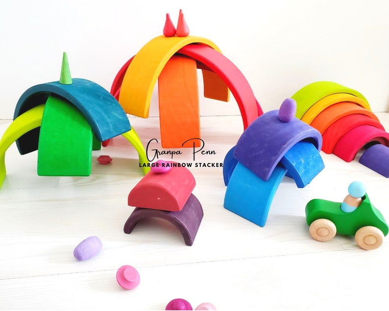 May include: A rainbow-colored wooden arch set with a green car and a small wooden figure. The set is made of natural wood and is perfect for imaginative play.