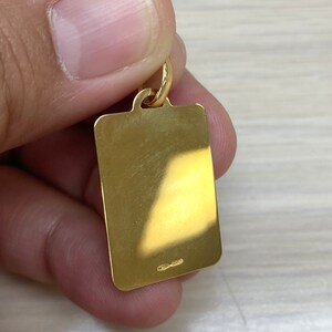Pode incluir: Um pingente retangular dourado com uma superf&iacute;cie lisa e um pequeno la&ccedil;o na parte superior. O pingente tem uma pequena inscri&ccedil;&atilde;o na parte inferior.