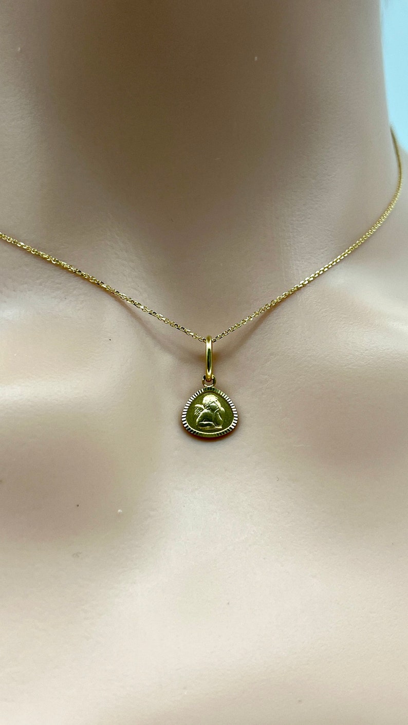 May include: A gold chain necklace with a small, round pendant featuring an angel design.