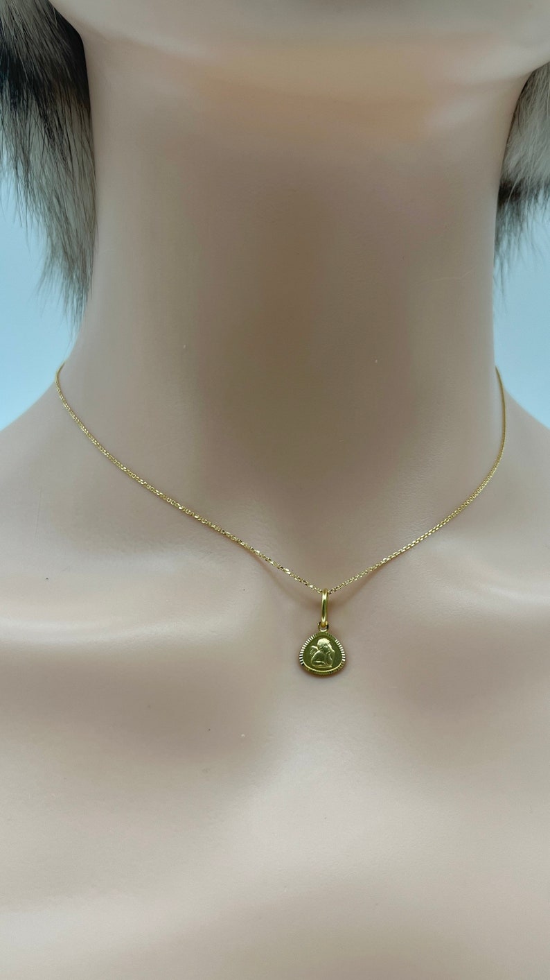 May include: A gold chain necklace with a small gold pendant featuring a detailed image of an angel.
