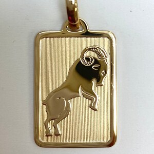 Pode incluir: Pingente de ouro com um design detalhado do signo do zod&iacute;aco &Aacute;ries, um carneiro com chifres encaracolados, sobre um fundo texturizado.