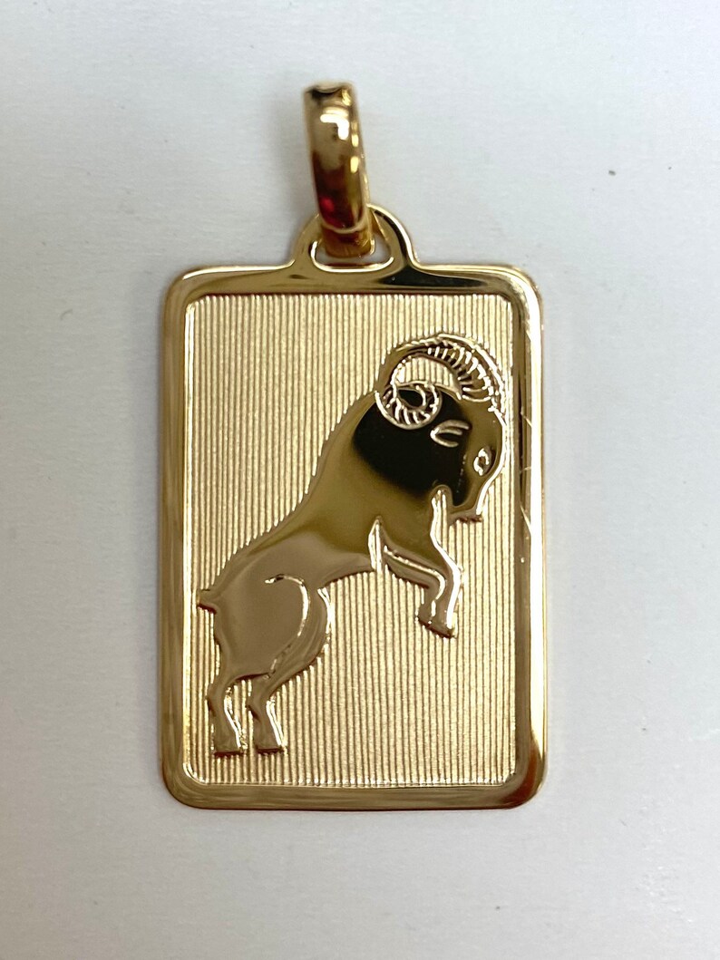 Pode incluir: Pingente de ouro com um design detalhado do signo do zod&iacute;aco &Aacute;ries, um carneiro com chifres encaracolados, sobre um fundo texturizado.