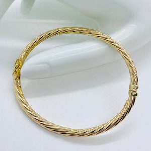 May include: A gold bangle bracelet with a twisted design. The bracelet is made of polished metal and has a simple, elegant look.