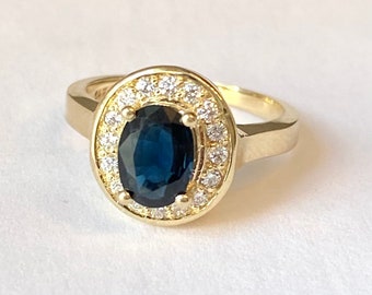 May include: A gold ring with a large oval blue sapphire surrounded by a halo of smaller white diamonds.