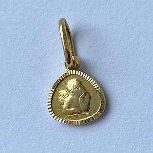 May include: A gold-colored pendant featuring a detailed image of a cherub angel with wings. The pendant is oval-shaped with a textured border.