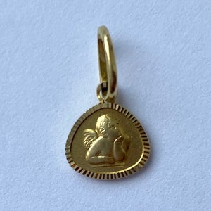May include: A gold pendant featuring a detailed image of a cherub angel with wings. The pendant is shaped like a teardrop and has a textured border.