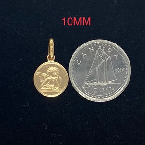 May include: A gold-colored pendant charm featuring a detailed depiction of a cherub angel with wings. The charm is 10mm in diameter and is shown next to a Canadian 10-cent coin for size comparison.
