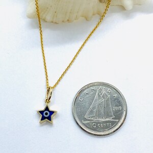 Może przedstawiać: Złoty łańcuszek z małym niebieskim i białym amuletem w kształcie gwiazdy z motywem złego oka. Amulet jest mniej więcej wielkości kanadyjskiej dziesięciocent&oacute;wki.
