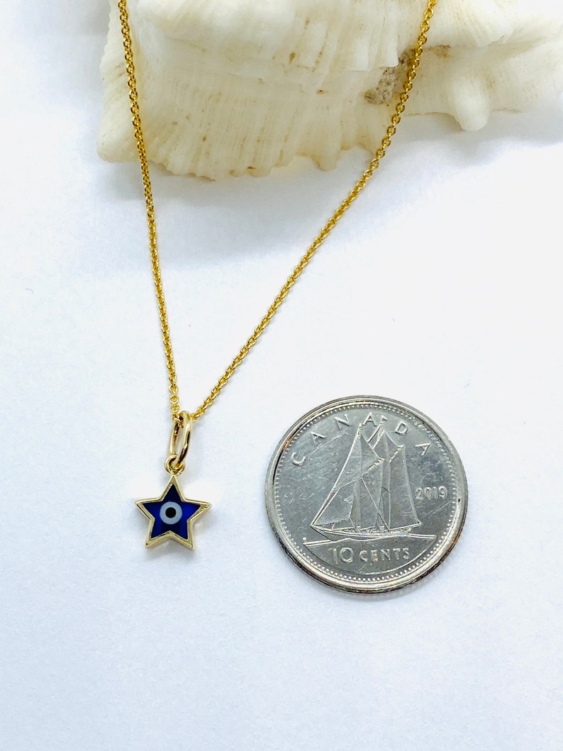 Może przedstawiać: Złoty łańcuszek z małym niebieskim i białym amuletem w kształcie gwiazdy z motywem złego oka. Amulet jest mniej więcej wielkości kanadyjskiej dziesięciocent&oacute;wki.