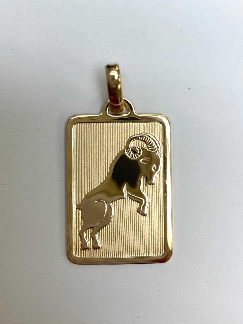 Pode incluir: Encanto de pingente de ouro com uma representa&ccedil;&atilde;o detalhada do signo do zod&iacute;aco &Aacute;ries, um carneiro com chifres encaracolados, sobre um fundo texturizado.