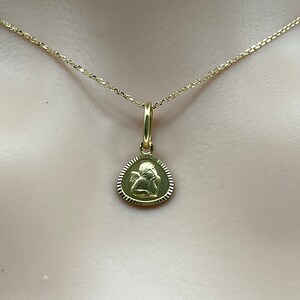 May include: A gold chain necklace with a small, round pendant featuring an angel design.