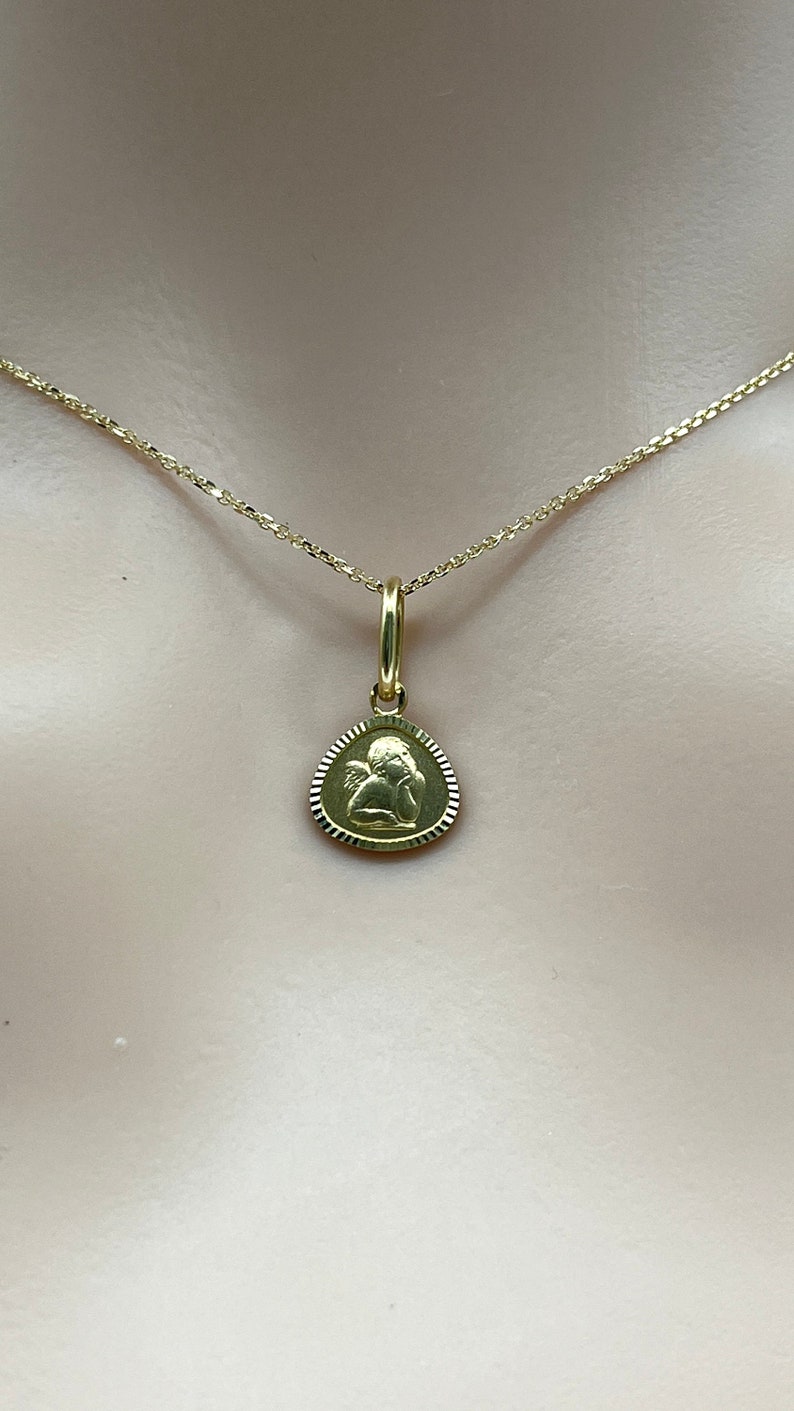 May include: A gold chain necklace with a small, round pendant featuring an angel design.