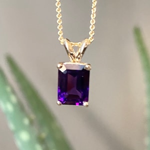 May include: A gold chain necklace with a pendant featuring a large, rectangular, deep purple amethyst gemstone.