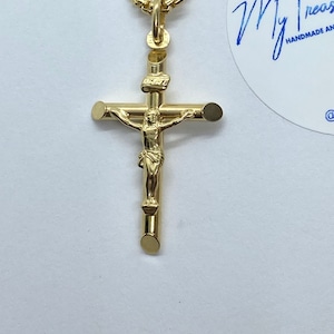 May include: A gold-tone pendant necklace featuring a crucifix with a small figure of Jesus Christ. The pendant is attached to a delicate chain.