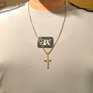 May include: A gold chain necklace with a gold cross pendant. The cross has a detailed design and a small figure of a person on it.