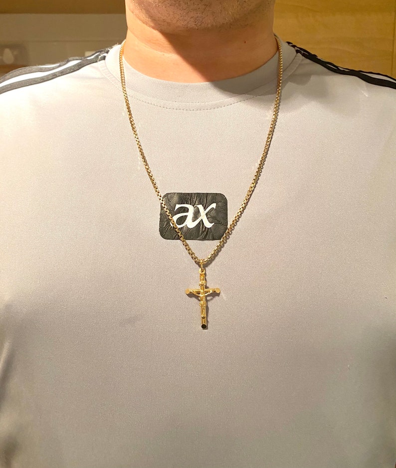 May include: A gold chain necklace with a gold cross pendant. The cross has a detailed design and a small figure of a person on it.