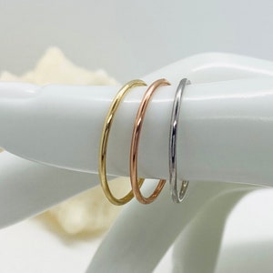 May include: Three thin gold rings, one yellow gold, one rose gold, and one white gold, stacked on a hand.