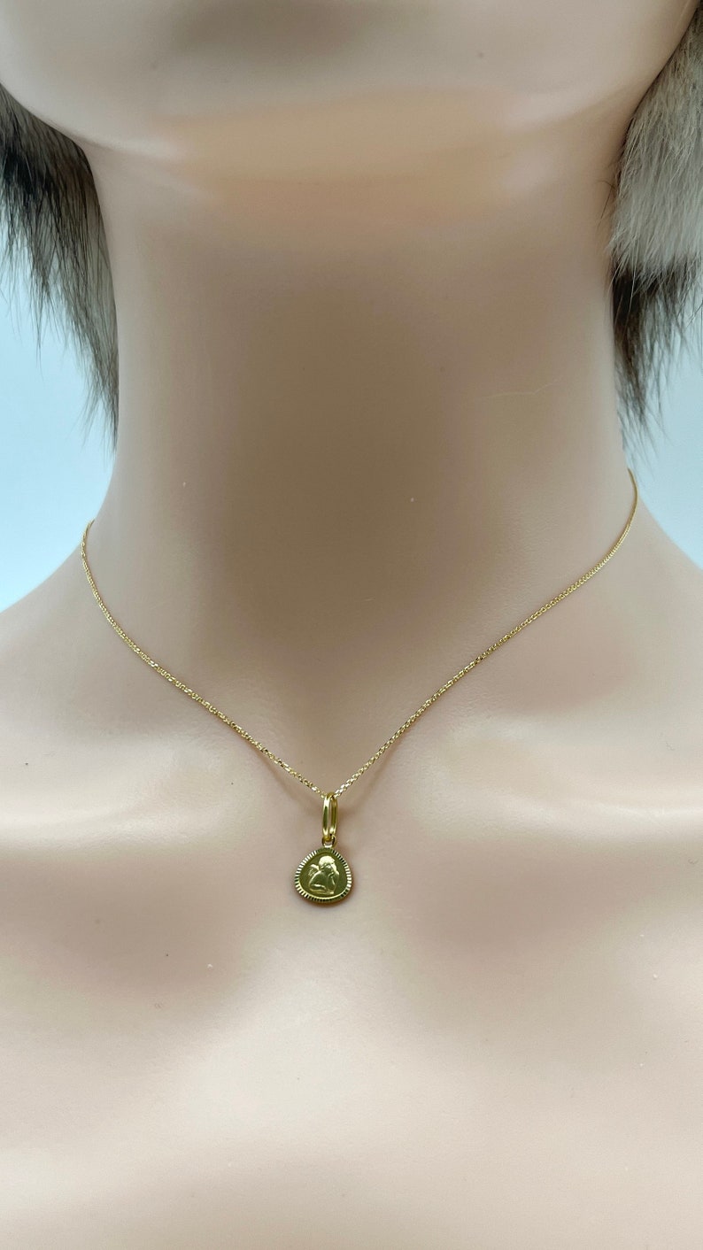 May include: A gold chain necklace with a small gold pendant featuring an angel design.