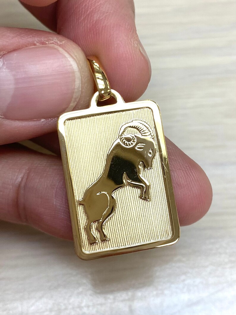 Pode incluir: Pingente dourado com uma representa&ccedil;&atilde;o detalhada do signo do zod&iacute;aco &Aacute;ries, o carneiro, dentro de uma moldura retangular.