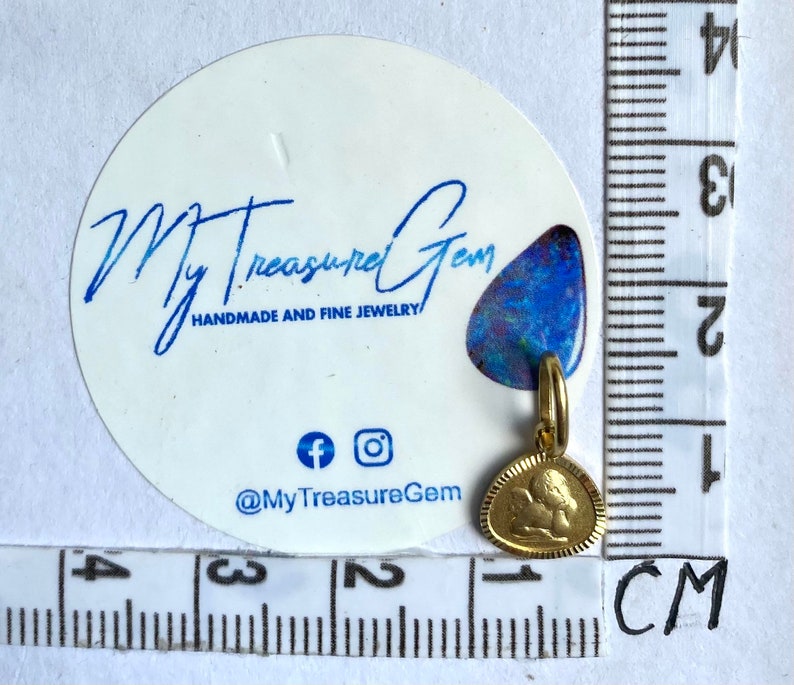 May include: Gold-toned pendant charm featuring a detailed angel design. The charm is approximately 1 cm in size and is shown next to a ruler for scale.