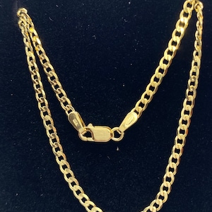 May include: A gold chain necklace with a curb link style. The chain is on a black background.