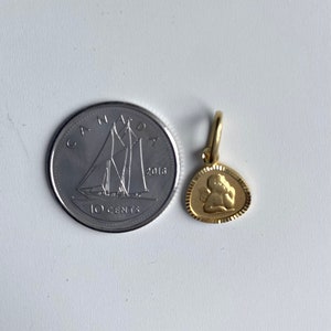 May include: A gold-colored angel charm pendant with a detailed design. The charm is about the size of a Canadian 10-cent coin.